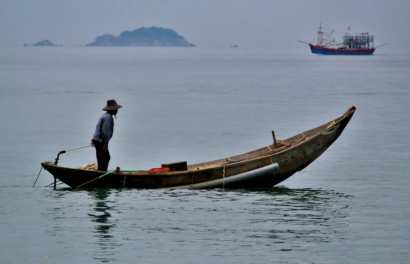 A fisherman standing in a wooden boat offshore near An Bàng Beach